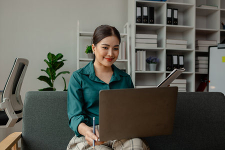 a businesswoman is using laptop in some area in workplace, she is meeting via video conference, a female employee is working in the office using laptop for typing some paperworkの写真素材