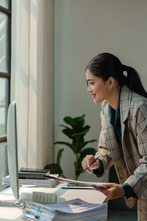 a businesswoman works at her desk, an entrepreneur is sitting and working in front of the computer to research for information on new project, female employee is in the officeの写真素材