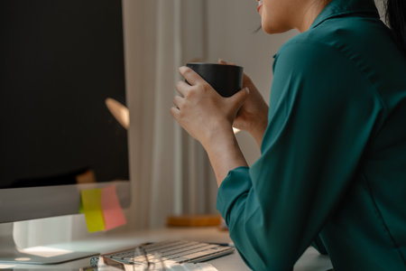 a businesswoman is in the conference meeting, a head of marketing department is listening her team present new marketing strategy plan via computer and holding a cup of coffeeの写真素材