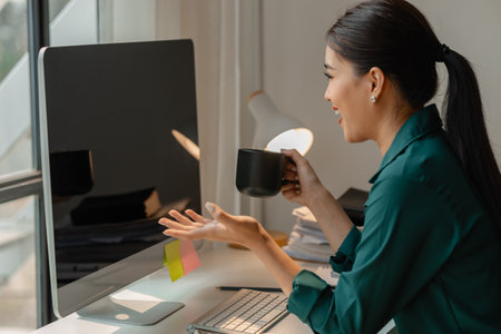 a businesswoman is in the conference meeting, a head of marketing department is listening her team present new marketing strategy plan via computer and holding a cup of coffeeの写真素材