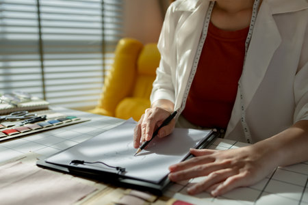 An Asian designer is sketching her idea of her new clothes collection to be stylish by using her creativity, a talented designer works on design a fashionable clothes for her brand as a professionalの写真素材
