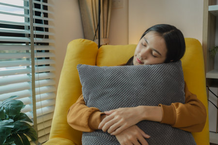 Asian woman sitting on the sofa in the living room, she is spending the weekend relaxing at home to relieve stress from hard work, full-time employee vacation.の写真素材