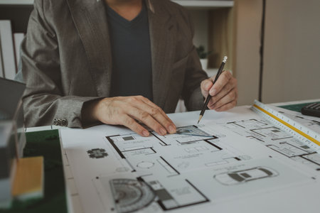 An architect is working in the office, there are blueprint and house model on the desk, engineer is...