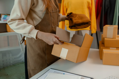 a beautiful female employee is packing clothing items into parcel box with great preparation following the correct procedures in order to deliver them to a customer's order, strong packagingの写真素材
