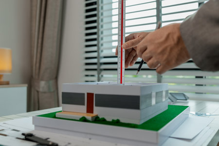 An architect works in the office, an engineer is using a tool to take measurements of a house model...