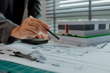 An architect is working in the office, there are blueprint and house model on the desk, engineer is checking overall of work that going to be present one last time, using tool for making work easierの写真素材