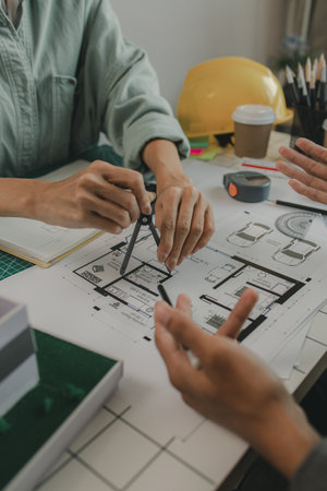engineers are sitting discussing a construction plan that needs to be revised to make the structure stronger, an architect and assistant are brainstorming and examining the blueprintsの写真素材