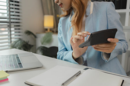 a businesswoman is using calculator in the office, checking company balance from paperwork, calculate finance information, calculating statistic marketing reportの写真素材