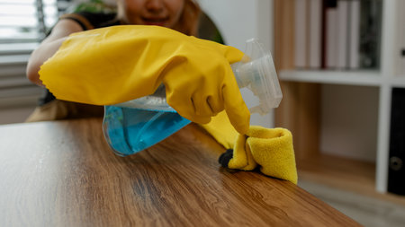 cleaning every single furnitures and decorations to keep them clean and neat before her parent back home, remove dust in living room with spray and towel, wearing gloves and apron.の写真素材