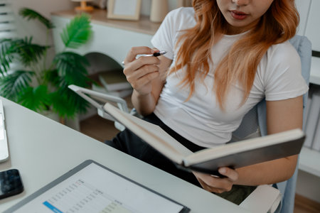 a businesswoman is working in her office and writing a note, a female employee is writing a brief summary of a report so that she will not forget, working in workplace while work hoursの写真素材