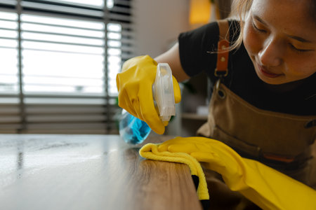 cleaning every single furnitures and decorations to keep them clean and neat before her parent back home, remove dust in living room with spray and towel, wearing gloves and apron.の写真素材