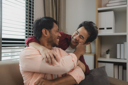 a male couple is spending time together happily in their living room, two handsome guys have a...
