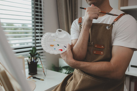a painter is in his painting studio, a rising male artist is focusing on creating his best paintings, both in drawing and painting, palette, canvas, paintbrush, oils, watercolors, poster colors.の写真素材