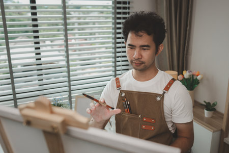 a painter is in his painting studio, a rising male artist is focusing on creating his best paintings, both in drawing and painting, palette, canvas, paintbrush, oils, watercolors, poster colors.の写真素材