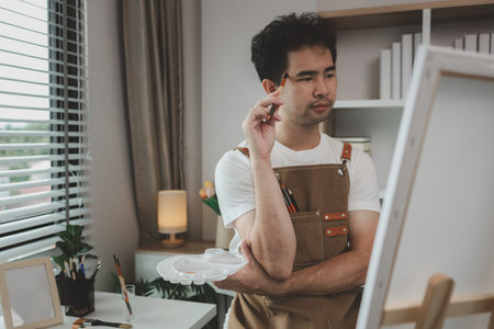 a painter is in his painting studio, a rising male artist is focusing on creating his best paintings, both in drawing and painting, palette, canvas, paintbrush, oils, watercolors, poster colors.の写真素材