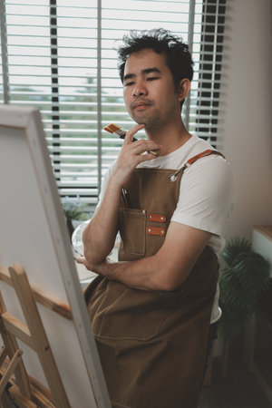 a painter is in his painting studio, a rising male artist is focusing on creating his best paintings, both in drawing and painting, palette, canvas, paintbrush, oils, watercolors, poster colors.の写真素材
