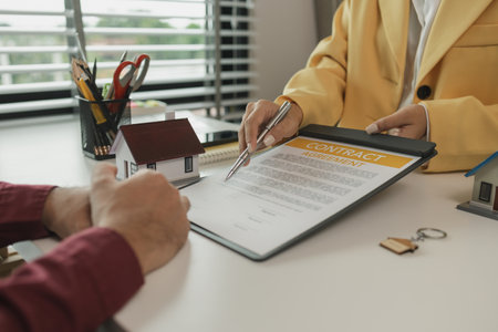 A man signs a contract after agreeing to buy a house with an agent. The agent explains the details of the contract to the buyer before signing it. Home purchase contractの写真素材
