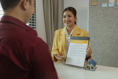 A man signs a contract after agreeing to buy a house with an agent. The agent explains the details of the contract to the buyer before signing it. Home purchase contractの写真素材