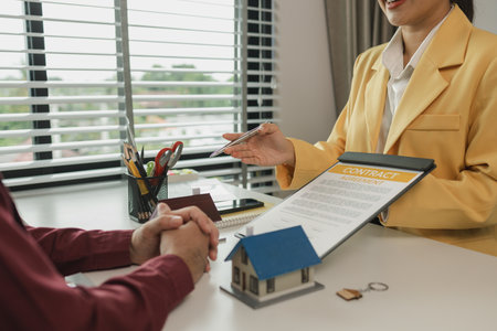 A man signs a contract after agreeing to buy a house with an agent. The agent explains the details of the contract to the buyer before signing it. Home purchase contractの写真素材