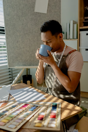 a fashion designer dis taking a break in his sewing studio after working all morning, a tailor is spending his free time in his workshop, which is filled with design and sewing equipmentの写真素材
