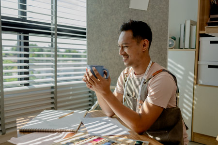 a fashion designer dis taking a break in his sewing studio after working all morning, a tailor is spending his free time in his workshop, which is filled with design and sewing equipmentの写真素材
