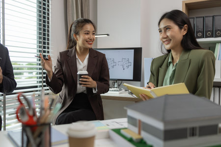Architects work with engineers and contractors in the office to check the accuracy of the first draft plan, blueprint on the desk, three architects are working together in the workplaceの写真素材