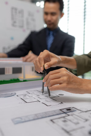 Architects work with engineers and contractors in the office to check the accuracy of the first draft plan, blueprint on the desk, three architects are working together in the workplaceの写真素材