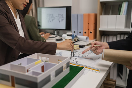 an architect is working in the office with his team, blueprint on the desk, contractor working with an engineer team, engineering and architecture, house model on the deskの写真素材