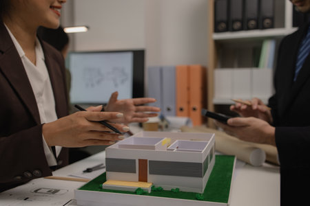 an architect is working in the office with his team, blueprint on the desk, contractor working with an engineer team, engineering and architecture, house model on the deskの写真素材