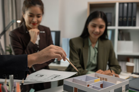 Architects work with engineers and contractors in the office to check the accuracy of the first draft plan, blueprint on the desk, three architects are working together in the workplaceの写真素材