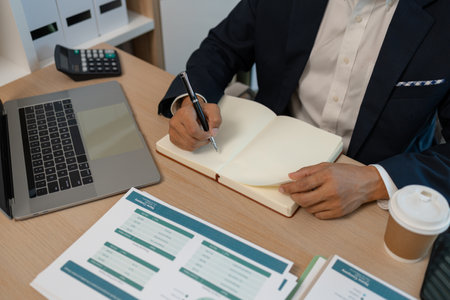 middle aged professional businessman wearing white shirt and suit happily smiling in office, a middle-aged, dark-haired businessman in a suit is happily working at his desk in the officeの写真素材