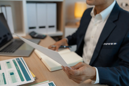middle aged professional businessman wearing white shirt and suit happily smiling in office, a middle-aged, dark-haired businessman in a suit is happily working at his desk in the officeの写真素材