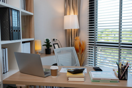 A sunlit office desk with an open laptop, productive workspace environment, cozy office with a stylish wooden desk, modern office space and professional work environment.の写真素材
