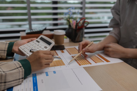 data analysis staff are helping to check data in various documents before summarizing and presenting them to the meeting, two business colleagues working together on paperwork at officeの写真素材