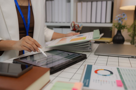 a businesswoman is using an electronic device to search and send information to her team, the marketing team leader is reviewing documents related to marketing dataの写真素材