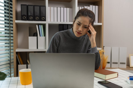 exhausted young woman with laptop in her home office, businesswoman, stress in office for project deadline, brain fog and frustrated with overtime, fatigue and overwhelmed for administrationの写真素材