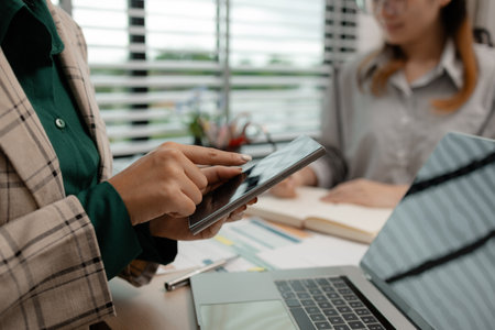 a businesswoman is using an electronic device to search and send information to her team, the marketing team leader is reviewing documents related to marketing dataの写真素材