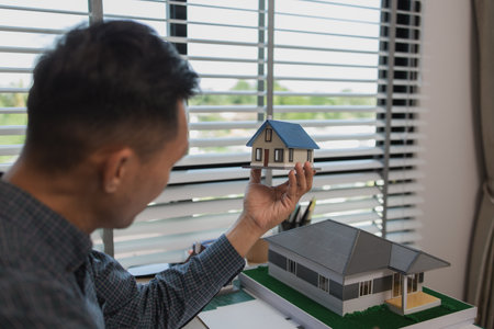 architect drawing and designing home, businessman or architect with model of a house sitting in office, Portrait of architect at workstation, architect looking at building model in officeの写真素材