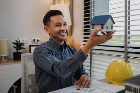 architect drawing and designing home, businessman or architect with model of a house sitting in office, Portrait of architect at workstation, architect looking at building model in officeの写真素材