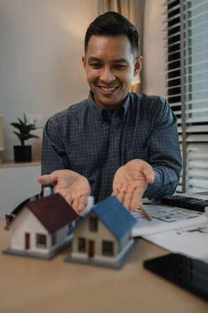 architect drawing and designing home, businessman or architect with model of a house sitting in office, Portrait of architect at workstation, architect looking at building model in officeの写真素材