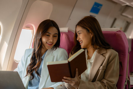 two beautiful businesswomen were traveling by plane to negotiate sales with their business partners abroad, while traveling they checked documents and worked to kill timeの写真素材