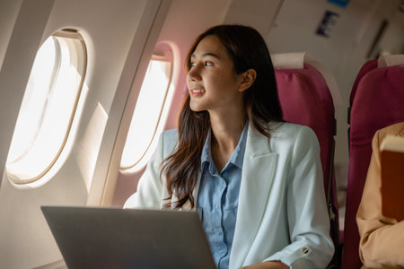 an asian woman is traveling abroad for vacation by plane, female traveler using her electronic device in an airplane to entertain herself, young woman flying abroad, journey, passenger, flightの写真素材
