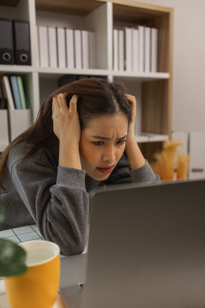 exhausted young woman with laptop in her home office, businesswoman, stress in office for project deadline, brain fog and frustrated with overtime, fatigue and overwhelmed for administrationの写真素材