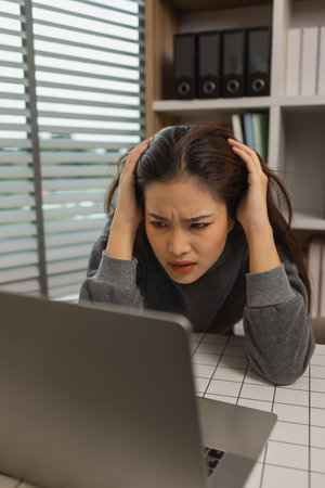 exhausted young woman with laptop in her home office, businesswoman, stress in office for project deadline, brain fog and frustrated with overtime, fatigue and overwhelmed for administrationの写真素材