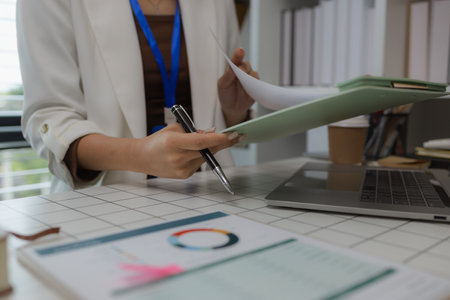 a businesswoman is sitting in her private office working on her desk with many documents to check, a lot of marketing documents were reviewed by the team leaderの写真素材