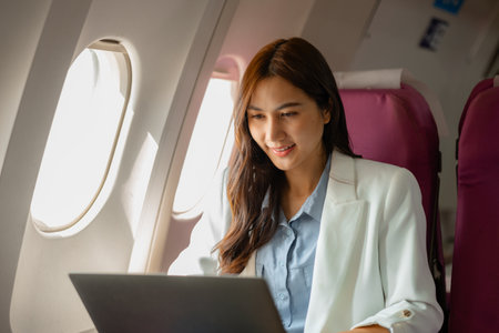 an asian woman is traveling abroad for vacation by plane, female traveler using her electronic device in an airplane to entertain herself, young woman flying abroad, journey, passenger, flightの写真素材