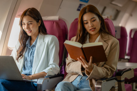 two beautiful businesswomen were traveling by plane to negotiate sales with their business partners abroad, while traveling they checked documents and worked to kill timeの写真素材