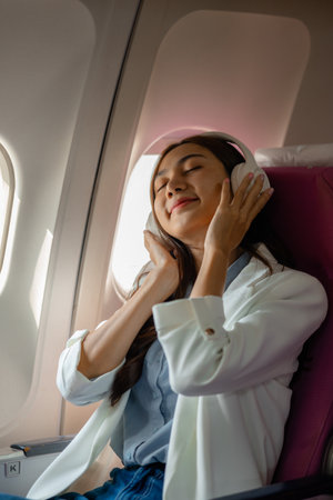 an asian woman is traveling abroad for vacation by plane, female traveler using her electronic device in an airplane to entertain herself, young woman flying abroad, journey, passenger, flightの写真素材