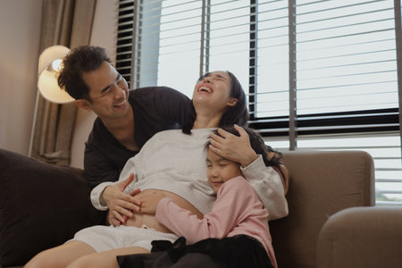 lovely family spend time together in their house, a pregnant mother sits on ;the couch with her...