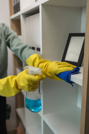 the wife is cleaning her husband home office, cleanup the room, wearing rubber glove to protect her...